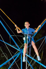 young boy having fun on rope jumping at reverse bungee trampoline at night