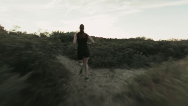 A cross country runner runs on a beach trail by sunset in the summer. Tracking footage.