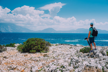 Male tourist with camera admiring breathtaking cloud scenery over the mountain range at the Mediterranean sea coast. Sunning outdoor scene of Ionian Islands, Kefalonia, Greece
