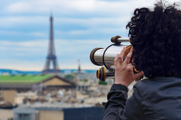 Beautiful brunette woman enjoying view by coin operated binoculars at Garnier Opera and Eiffel Tower in Paris, France