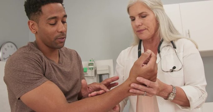 Portrait of young black male consulting with female senior doctor about wrist pain. Close up of african-american male talking to mature doctor about arm injury