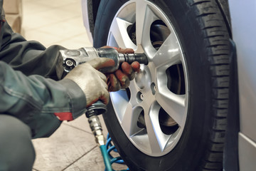 Replacing summer tires for winter using pneumatic wrench tool by mechanic worker after balancing...