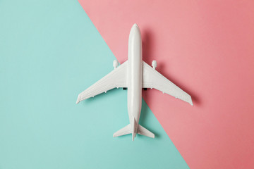 Simply flat lay design miniature toy model plane on blue and pink pastel colorful paper trendy geometric background. Travel by plane vacation summer weekend sea adventure trip concept
