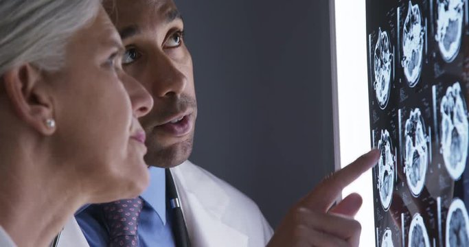 Tight shot of millennial african-american doctor discussing with senior colleague patient ct scans. Close up of two medical physicians consulting over xrays of cranium