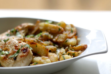 Roasted chicken and Lyonnaise potatoes. Lyonnaise potatoes are sliced pan-fried potatoes with onion, parsley, butter and garlic. Selective focus.