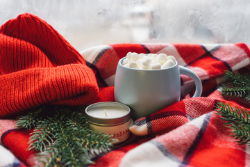 Hot coffee cup with marshmellows on the window with Christmas candle and decoration on frosty winter day. Christmas holiday mood concept. Cozy winter background