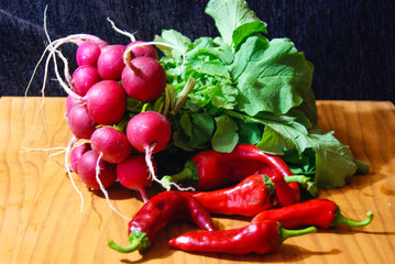 Red radishes and red peppers over wood tabke and black background