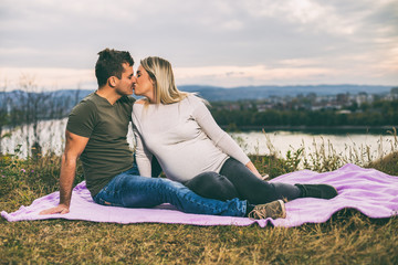 Naklejka na ściany i meble Husband and his pregnant wife kissing while they enjoy spending time together outdoor.