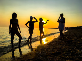 group of happy young people dancing at the beach on beautiful summer sunset