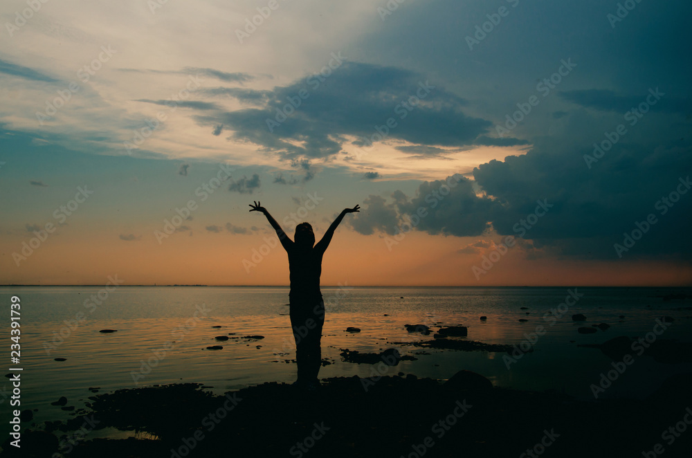 Wall mural silhouette of a woman at dusk on the beach against the late sunset