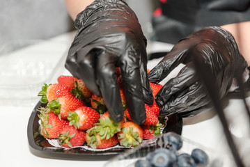 The girl puts strawberries on a plate. Juicy bright fresh strawberries on a plate.