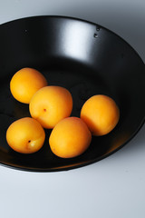 A bunch of peaches lying on a black plate. Close up view. Pastel apricot colors, minimal trendy concept art.