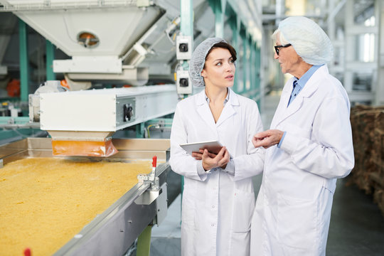 Portrait  of  two  female workers doing  production quality inspection in food factory standing by conveyor belt and using digital tablet, copy space