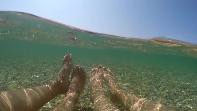Couple on summer vacation exchange love emotions sitting in shallow sea water with peebles, stones