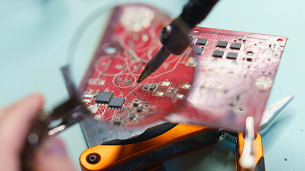 Repair motherboard. Magnifying glass shows close-up of part of microcircuit and soldering iron. Man...