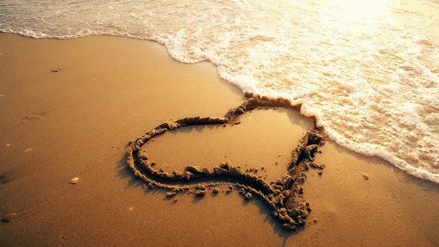 Summer romantic vacation concept of hearth on sand being washed by sea waves at sunset