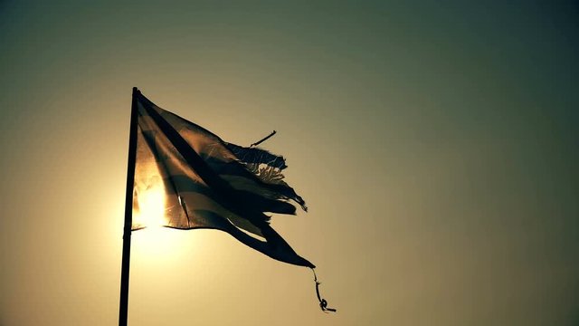 Greek flag waving on beach against sunset sun