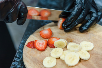 The girl cuts the fruit on the board with a knife. Fruits sliced. Cooking fruit salad.