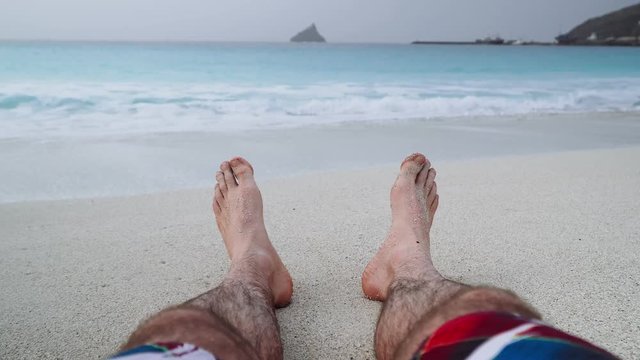 Mans feet on sandy beach. Vacation and relaxation concept, beach holidays background. 4k video