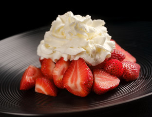 Strawberries with cream on a black plate