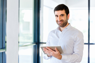 Young handsome businessman using his touchpad standing in office