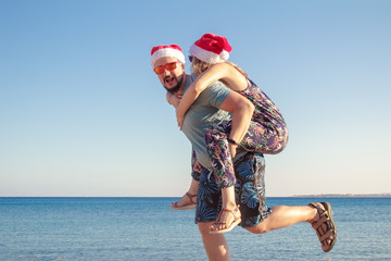 piggybacking family in christmas hats and sunglasses at the beach of the sea