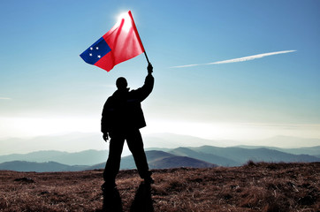 Successful silhouette man winner waving Samoa flag on top of the mountain peak