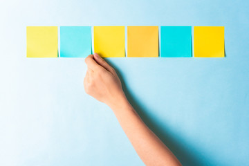 Assessment analysis evaluation concept. Hand choosing multi colored notes on blue background.