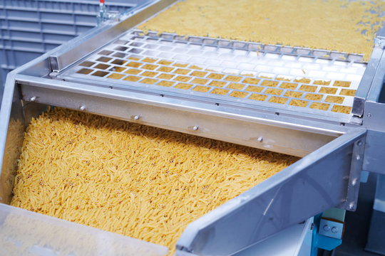 Closeup Shot Of Dry Macaroni Spilling From Machine Unit On Modern Food Production Factory, Copy Space