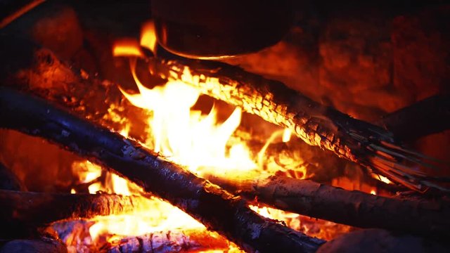 Closeup view of burning firewoods, firecamp with sparks and black pot above it