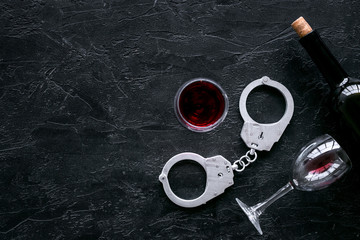 Illegal sale of alcohol concept. Handcuffs near wine glass and bottle on black background top view copy space