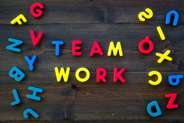 Teamwork training concept. Text teamwork lined with colored letters near toy letters on dark wooden background top view space for text
