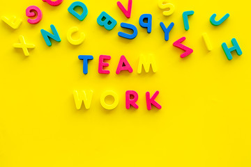 Teamwork training concept. Text teamwork lined with colored letters near toy letters on yellow background top view copy space