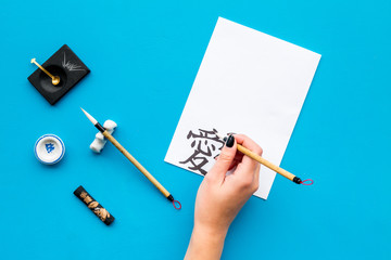 Calligraphy. Hand writes hieroglyph on white paper on blue background top view copy space