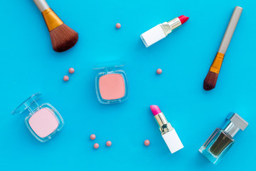 Set of pink cosmetics. Lipstick, bulk, eyeshadow, perfume near brushes on blue background top view