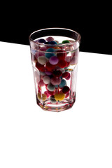 Unusual photo of a glass with water and colored balls on a black and white background.