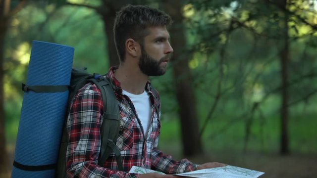 Confused hiker lost in forest tries to read map for directions, emotional stress