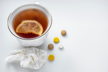 Tea with lemon, pills and handkerchief on the white table. The concept of colds.