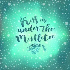Kiss Me Under The Mistletoe. Christmas quote calligraphic greeting card on winter sky northern lights background with stars
