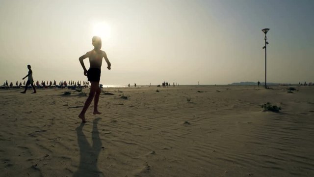 Trekking chase of a young boy running away on empty beach sand at sunrise, cinematic steadicam shot