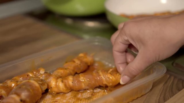 Female hand frying skewers of meat cooked on a spit in a pan