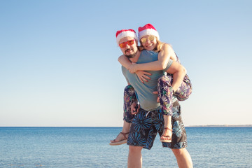 piggybacking in christmas hats and sunglasses at the beach of the sea