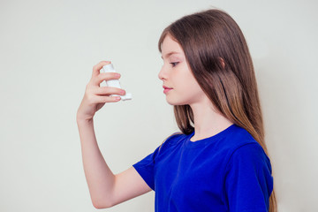 Young teen girl woman using asthma inhaler at home against a white wall background