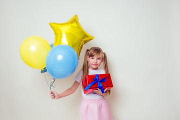 cute little girl holding helium blue, yellow and gold balloons and a box with a gift happy Birthday on white background in studio .christmas and new year holiday