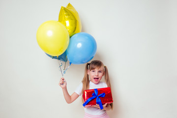 Fototapeta na wymiar cute little girl holding helium blue, yellow and gold balloons and a box with a gift happy Birthday on white background in studio .christmas and new year holiday