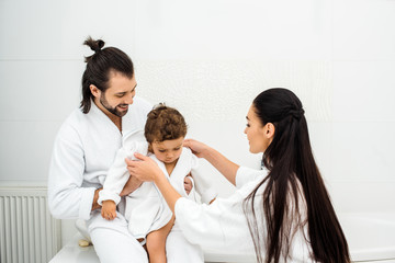 Parents smiling and looking at toddler son in white bathrobe