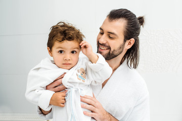 Dad looking at toddler son in white bathrobe and smiling