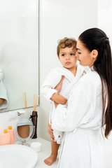 beautiful mother and cute son in white bathrobes in bathroom