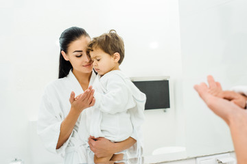 Fototapeta premium mother in white bathrobe gently holding son hand