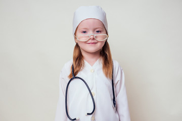 Adorable child girl uniformed as doctor wearing doctor's cap and glasses with stethoscope on white background.Happy kid little female doctor career guidance dreaming about future profession